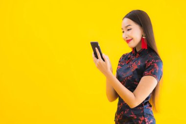 Güzel bir portre genç Asyalı kadın Çin elbisesi giyer Çin 'in yeni yıl konsepti için sarı izole edilmiş arka planda akıllı cep telefonu kullanır.