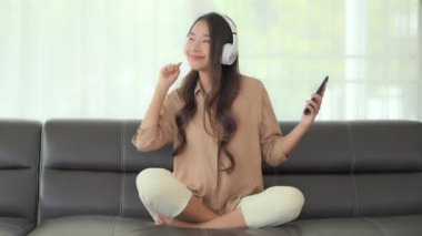 Güzel Asyalı bir kadının akıllı telefon ve kulaklıkla müzik dinlediği görüntüler.
