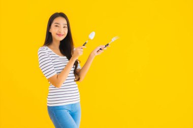 Güzel Asyalı genç bir kadının portresi sarı izole edilmiş arka planda kaşığı ve çatalı yemeye hazır gösteriyor.