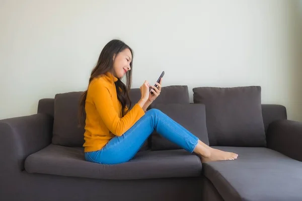 在客厅内用带枕头的沙发上用智能手机描绘年轻的亚洲女人 — 图库照片