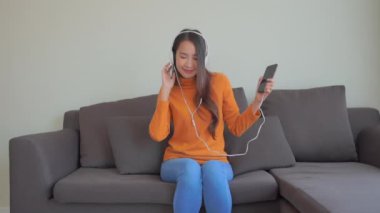 Güzel Asyalı bir kadının akıllı telefon ve kulaklıkla müzik dinlediği görüntüler.