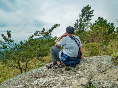 Tayland 'ın Sukhothai bölgesindeki Ramkhamhaeng Ulusal Parkı' ndaki Khao Luang dağındaki taşın üzerinde oturan Asyalı Şişko Trekker.