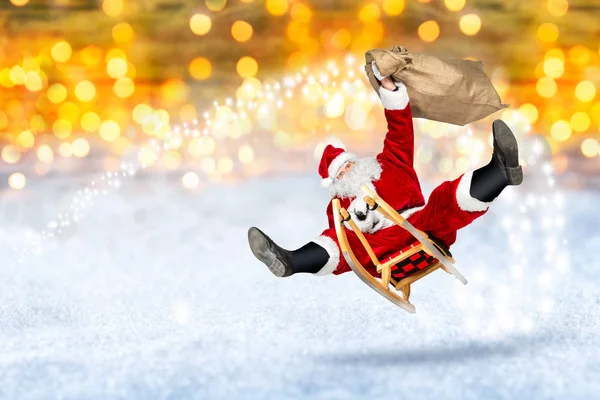 疯狂的圣诞老人在他的雪橇上飞行与袋的礼物在雪地明亮的金色灯光散景背景 — 图库照片