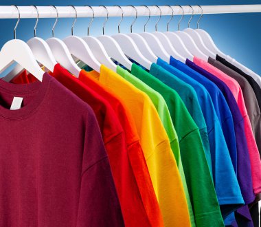 Renkli gökkuşağı renklerinde bir sürü yeni kumaş pamuk t-shirt 'ler gardıropta asılı. Mavi beyaz arka planda çeşitli renkli gömlekler. diy printing moda konsepti.