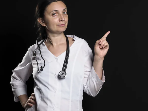 Médico feminino mostra gestos de mão e posa em um fundo preto — Fotografia de Stock