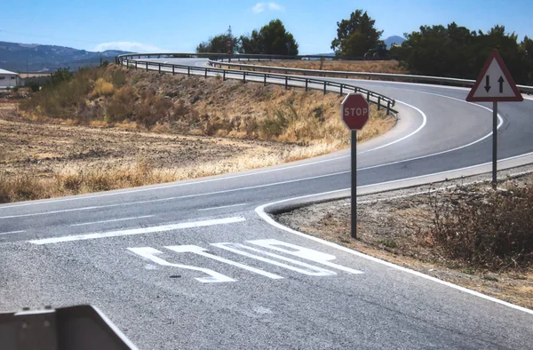 Kırsal bir bölgede iki yönlü bir kavşakta dur işareti ve işaretler var.