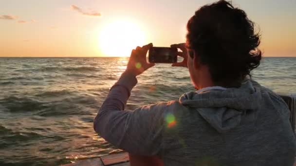 Ung vuxen tar tre bilder av solen faller över horisonten — Stockvideo