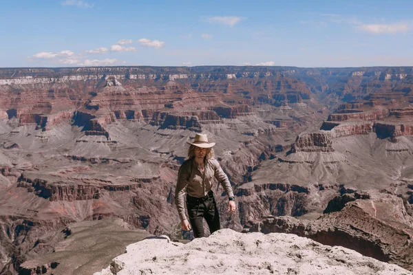 Kıvırcık saçlı sarışın bir adam, bej tişört, siyah kot pantolon, siyah ayakkabılar, bej keten gömlek ve uyumlu kovboy şapkası, Grand Canyon manzarası — Stok fotoğraf