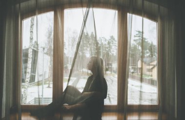 Siluetli sarışın kız pencere eşiğinde oturuyor.