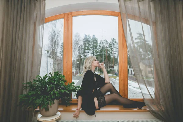 Γυναίκα κοιτάζει μέσα από το παλιό παράθυρο κάθεται στο περβάζι του παραθύρου. Ντυμένες με κάλτσες — Φωτογραφία Αρχείου