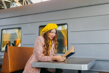 Harika bir kızın portresi, ceketli ve sarı bereli. Tren istasyonunda oturmuş bir kitap okuyor ve dümdüz bakıyordu. Sonbahar konsepti.