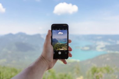 Deniz ve dağlarda cep telefonu tutan bir adam. Fotoğrafı doğadaki turist çekiyor.