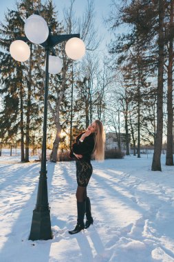 Sokak lambası altında kırmızı dudakları olan, poz veren ve güneşi izleyen bir manken. Arka planda güneş ışığı var. Kar yağıyor.