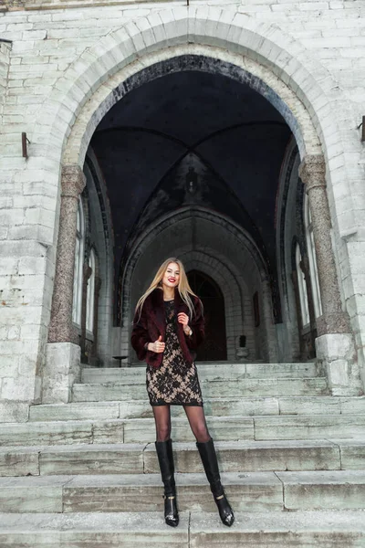 若い女の子は毛皮のコートを着て立って服を着て 教会の階段をまっすぐ見てください 背景にある古い教会 — ストック写真