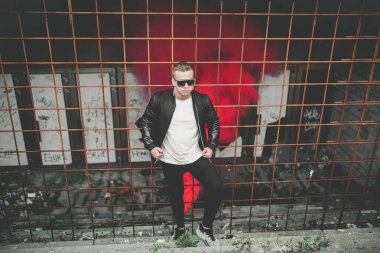 Sokakta elinde sis bombasıyla duran deri ceketli bir adam. Kırmızı duman bombası taşıyan Avrupalı gencin renkli portresi