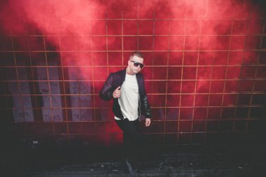 Sokakta elinde sis bombasıyla duran deri ceketli bir adam. Kırmızı duman bombası taşıyan Avrupalı gencin renkli portresi