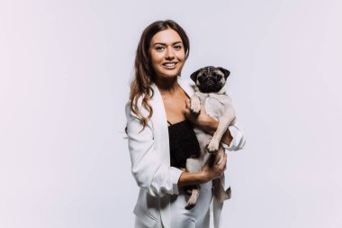 Beyaz elbiseli, gülen ve gülümseyen kumral saçlı bir kadın, sakince elleri üzerinde oturan ve tüm dikkatini toplayan sevimli köpeğine sevgiyle bakıyor. İzole edilmiş beyaz arkaplan