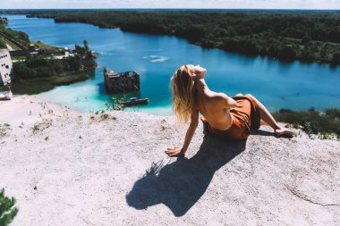 Rummu taş ocağının pitoresk bir noktasında, sarışın bir kadın çıplak ayakla ayakta duruyor, yüksek, kumral renkli bir elbise giyiyor, ve kameraya arkasını dönüyor. Temiz Su