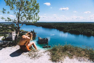 Rummu taş ocağının pitoresk bir noktasında, sarışın bir kadın oturuyor, uyluk yüksekliğinde, kumral renkli bir elbise giyiyor, ve kameraya arkasını dönüyor. Temiz Su