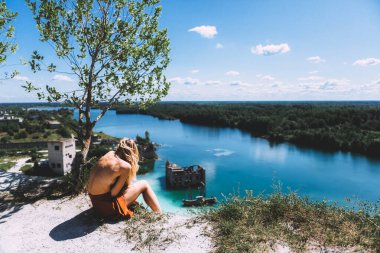Rummu taş ocağının pitoresk bir noktasında, sarışın bir kadın oturuyor, uyluk yüksekliğinde, kumral renkli bir elbise giyiyor, ve kameraya arkasını dönüyor. Temiz Su