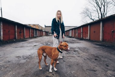 Uzun saçlı, spor takım elbiseli, beyaz ceketli. Bir pitbulu geniş bir tasma zincirinden nazikçe tutmak. Eski garajlarda poz vermek