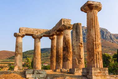 Korint Yunanistan 'daki Apollo Tapınağı harabeleri dağ atlılarıyla dolu parlak bir güneşin altında kaya duvarlarının kalıntılarıyla bir tepenin üzerinde duruyor..