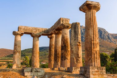 Korint Yunanistan 'daki Apollo Tapınağı harabeleri dağ atlılarıyla dolu parlak bir güneşin altında kaya duvarlarının kalıntılarıyla bir tepenin üzerinde duruyor..