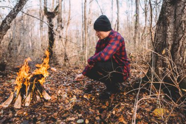 Kamp ateşinin yanında oturan ve atmosferin tadını çıkaran bir adam.