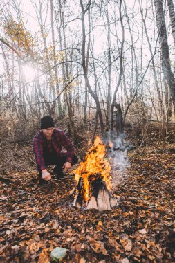 Kamp ateşinin yanında oturan ve atmosferin tadını çıkaran bir adam.
