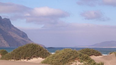 Plaj ve Dağlar - Caleta de Famara 'nın güzel kıyıları, Lanzarote Kanarya Adaları. Caleta de Famara 'daki plaj sörfçüler arasında çok popüler..
