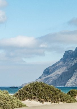 Plaj ve Dağlar - Caleta de Famara 'nın güzel kıyıları, Lanzarote Kanarya Adaları. Caleta de Famara 'daki plaj sörfçüler arasında çok popüler..
