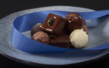 A bunch of exquisite chocolate cubes, embellished with blue ribbons, placed on a dark blue ceramic plate with parallel stripes.