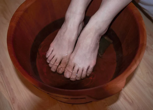 A woman soaks her feet in a deep reddish brown foot bath