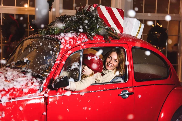 Christmas. Mom with daughter laughing in a red car under the snow