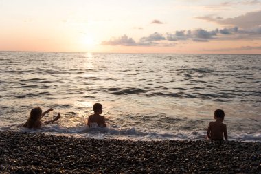 Mutlu çocuklar gün batımında deniz dalgalarında oynuyorlar  