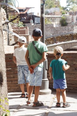 Şehirde yürüyen üç çocuğun arka görüntüsü.