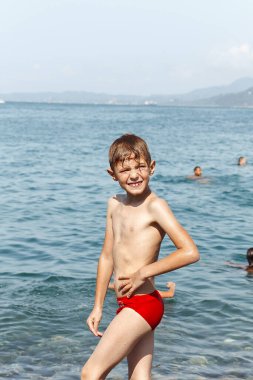 Çocuk denizde duruyor ve gülümsüyor.