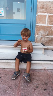 Küçük tatlı çocuk merdivenlerde oturuyor ve dondurma yiyor.