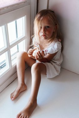 Beyaz penceredeki üzgün küçük bir kızın portresi.