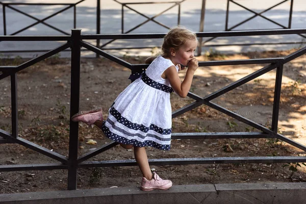 Egy Kislány Fehér Ruhában Fém Kerítésen Játszik Utcán — Stock Fotó