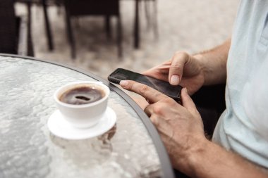 Kafede kahve ve telefonla oturan sakallı bir adam.