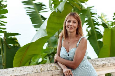 Büyük bitki yapraklarının yanında duran bir kadın.