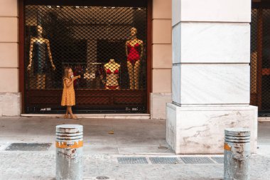 Sarı elbiseli küçük kız dükkanlarda dolaşıyor.