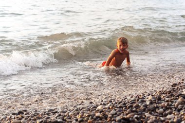 Küçük çocuk gün batımında denizde yüzüyor.