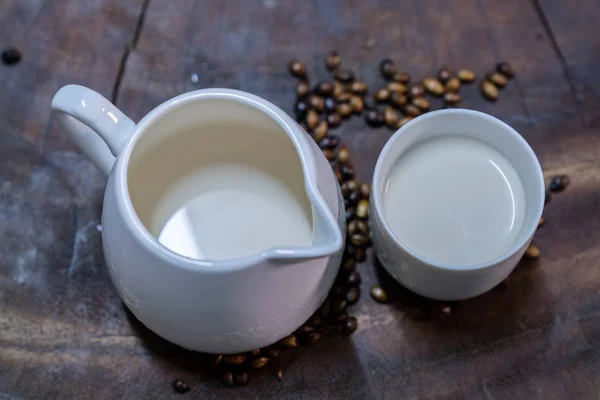 La leche fresca se coloca en un vaso blanco colocado en una mesa de madera vieja . —  Fotos de Stock