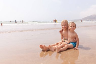 Plaj okyanus deniz üzerinde oturan iki sevimli sevimli küçük kardeşler erkek