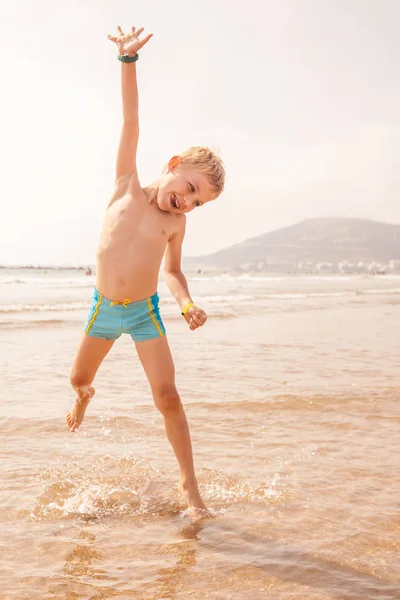 Μικρό αγόρι παίζει με τα κύματα στη θάλασσα σε μια ηλιόλουστη ημέρα — Φωτογραφία Αρχείου