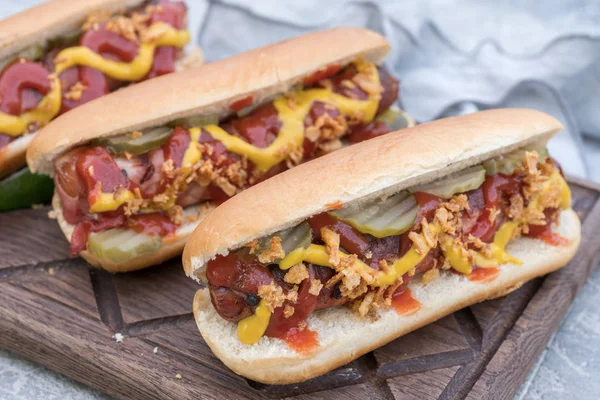 Hot Dog mit Speckwürstchen, Ketchup, gelbem Senf, gebratenen Zwiebeln und Essiggurken — Stockfoto