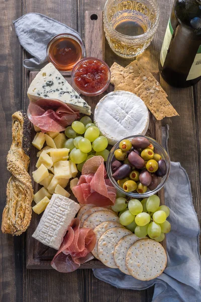 Сырная тарелка подается с виноградом, джемом, ветчиной, крекерами на деревянном фоне — стоковое фото