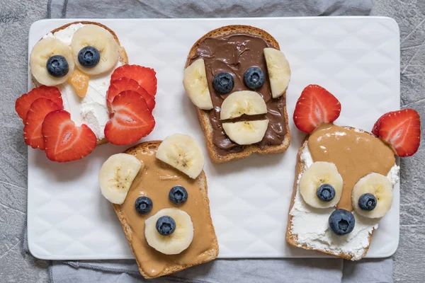 Funny animal faces toasts with banana, strawberry and blueberry